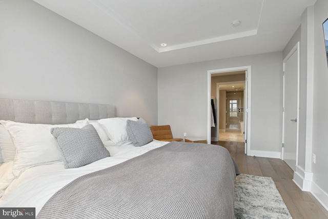 bedroom with baseboards, a tray ceiling, recessed lighting, and wood finished floors