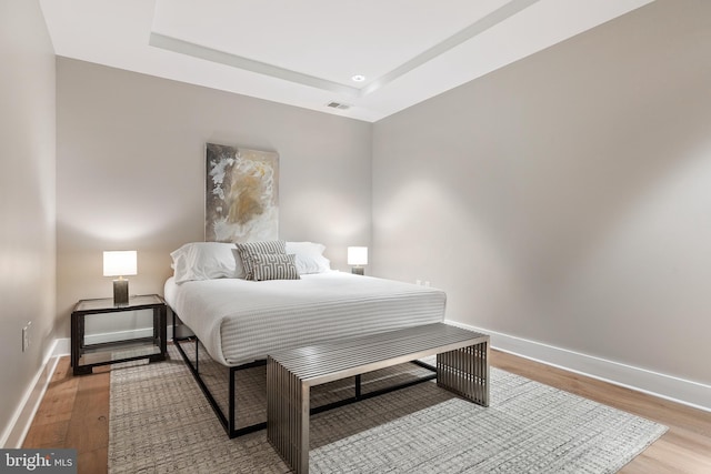 bedroom featuring baseboards, a tray ceiling, light wood-type flooring, and visible vents