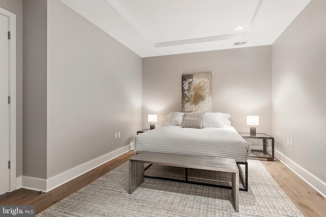 bedroom featuring baseboards, wood finished floors, a tray ceiling, and visible vents