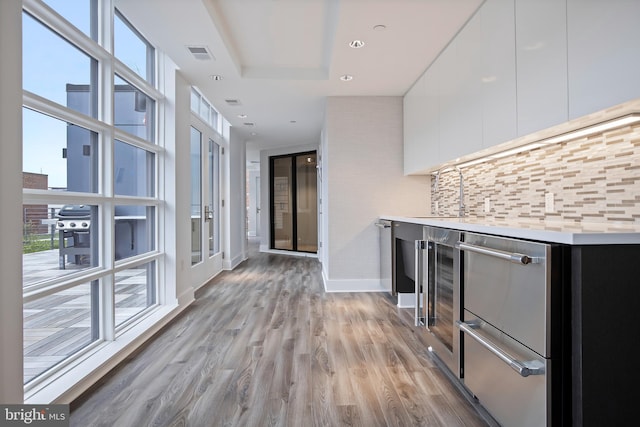 hallway with a sink, beverage cooler, light wood-style flooring, baseboards, and visible vents