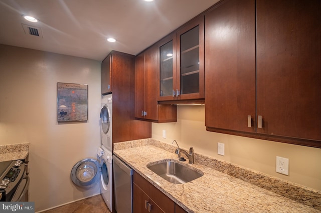 kitchen with stacked washer / drying machine, light stone counters, a sink, stainless steel appliances, and visible vents