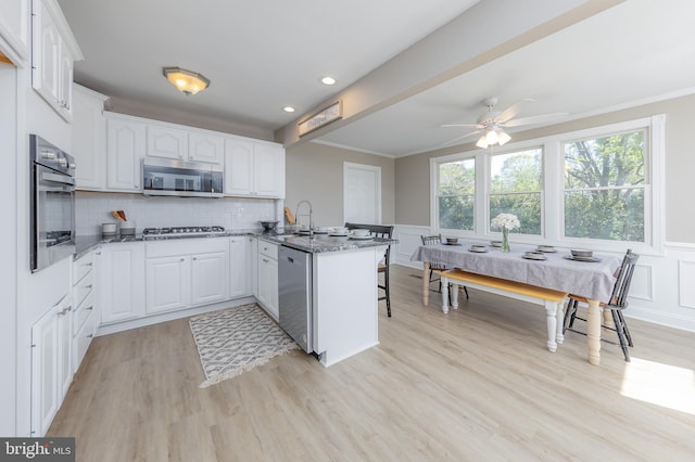 kitchen featuring white cabinets, appliances with stainless steel finishes, light wood-style floors, dark stone countertops, and a peninsula