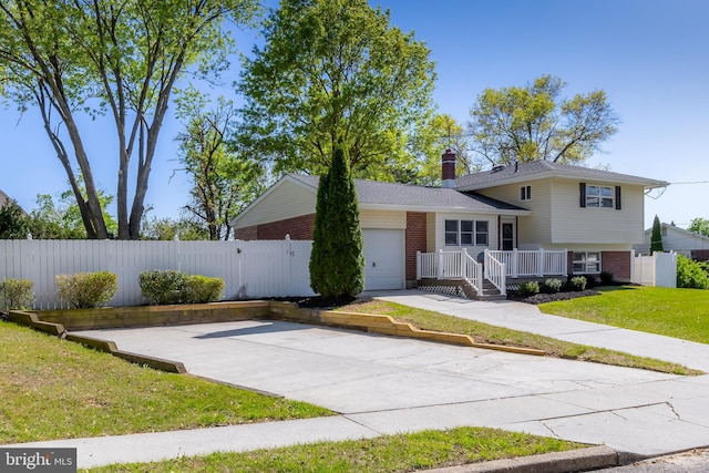 split level home featuring brick siding, an attached garage, fence, and a chimney