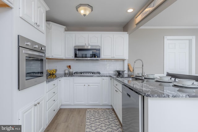 kitchen featuring a sink, dark stone counters, stainless steel appliances, white cabinetry, and a peninsula