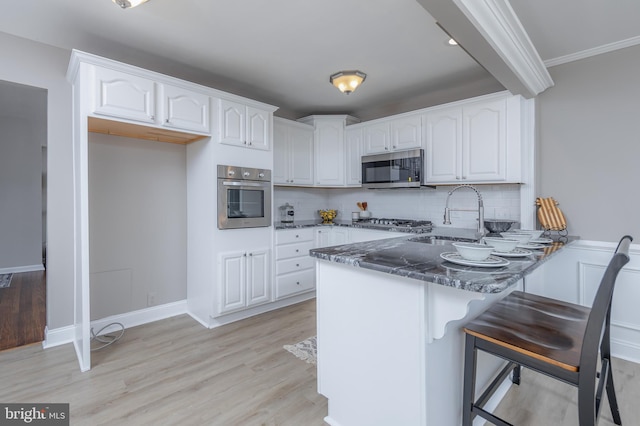 kitchen with white cabinets, appliances with stainless steel finishes, a sink, dark stone counters, and a peninsula