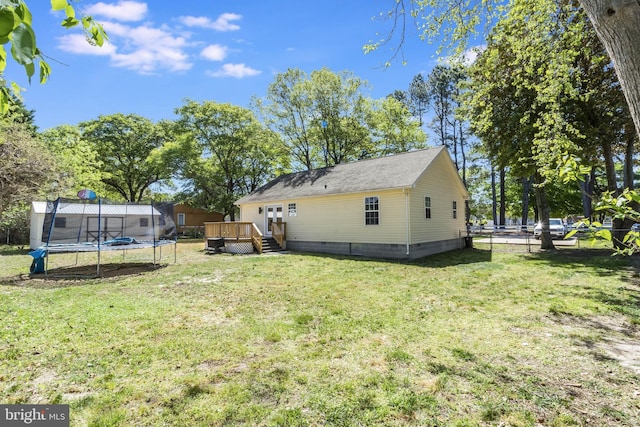 back of property featuring crawl space, a trampoline, a lawn, a wooden deck, and fence