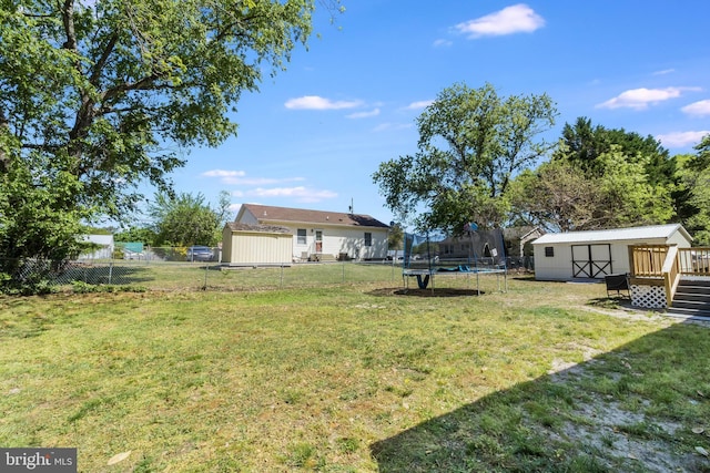 view of yard with a trampoline, a storage shed, an outbuilding, a wooden deck, and a fenced backyard