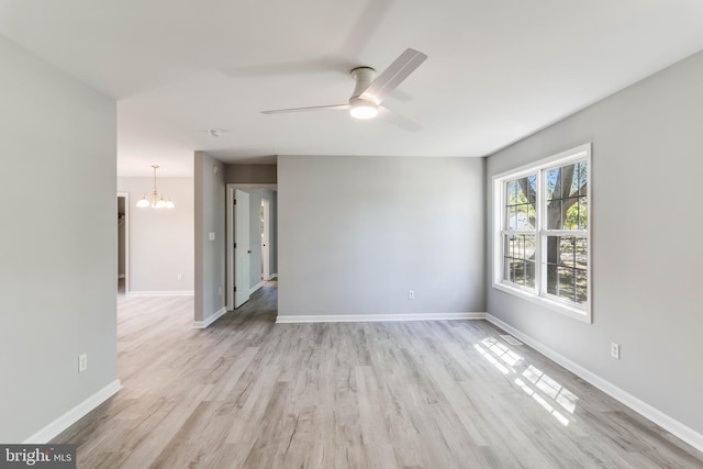 unfurnished room featuring baseboards, ceiling fan with notable chandelier, and light wood finished floors