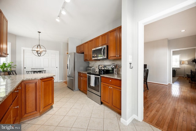 kitchen featuring a notable chandelier, baseboards, decorative backsplash, brown cabinets, and appliances with stainless steel finishes