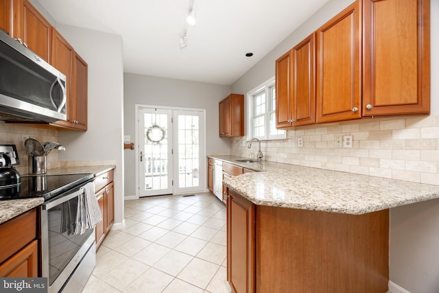 kitchen with brown cabinetry, baseboards, light tile patterned floors, a sink, and appliances with stainless steel finishes