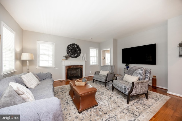 living area featuring wood finished floors, baseboards, and a brick fireplace