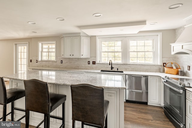 kitchen featuring light stone countertops, a sink, stainless steel appliances, decorative backsplash, and a kitchen bar