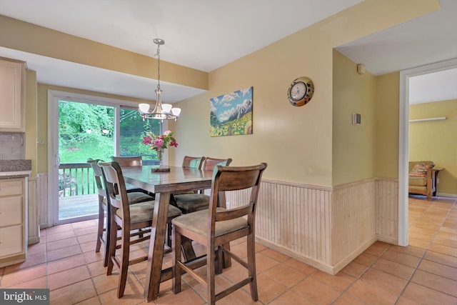 dining area featuring light tile patterned floors, a chandelier, and a wainscoted wall