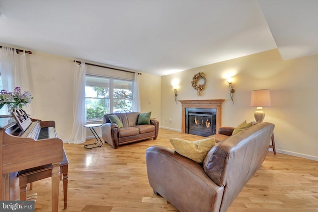 living area with baseboards, light wood-type flooring, and a glass covered fireplace