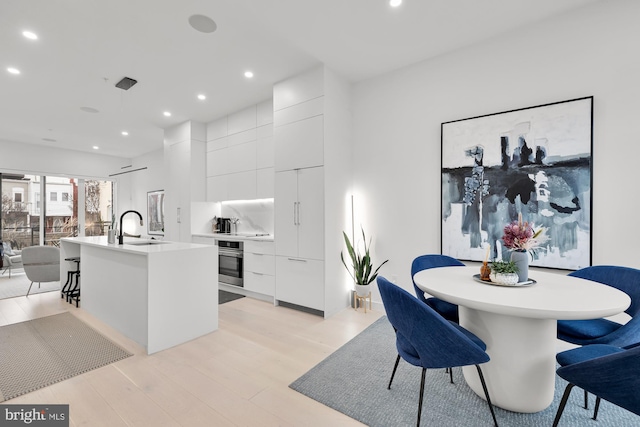 kitchen with oven, modern cabinets, a center island with sink, recessed lighting, and a sink