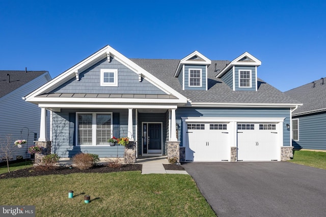 craftsman house with a shingled roof, an attached garage, a front lawn, stone siding, and aphalt driveway