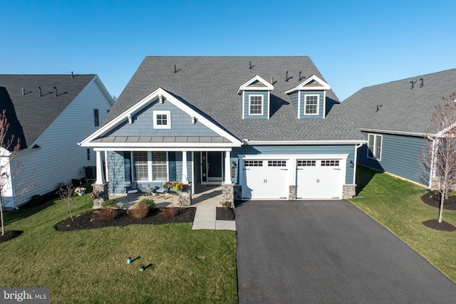 view of front of home with covered porch, stone siding, a front yard, a shingled roof, and driveway