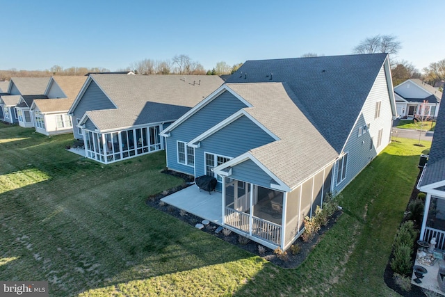 rear view of house featuring roof with shingles, a yard, a patio, and a sunroom