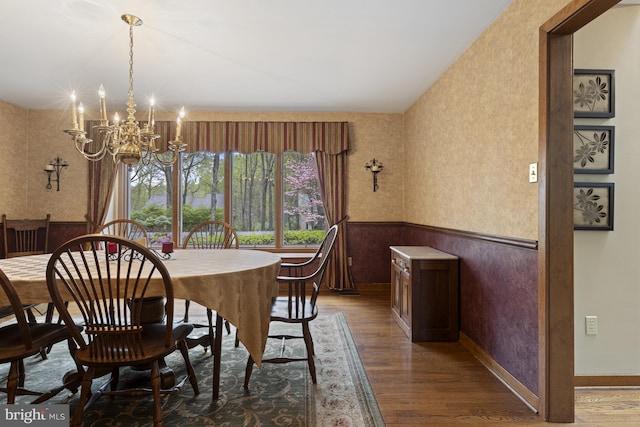 dining area featuring an inviting chandelier, wood finished floors, vaulted ceiling, and a wainscoted wall