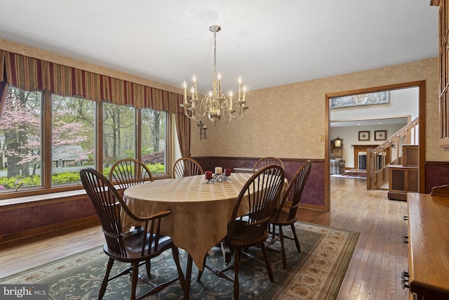 dining area with wood-type flooring, an inviting chandelier, wainscoting, and stairway