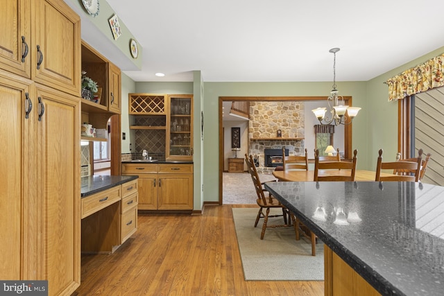 kitchen featuring open shelves, a stone fireplace, a chandelier, light wood-style flooring, and hanging light fixtures