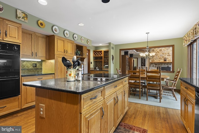 kitchen featuring decorative backsplash, wood finished floors, a kitchen island, black appliances, and a notable chandelier