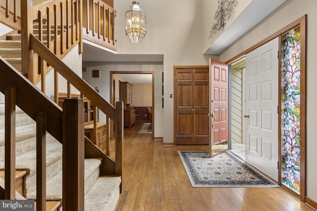 foyer with an inviting chandelier, stairs, baseboards, a high ceiling, and hardwood / wood-style flooring