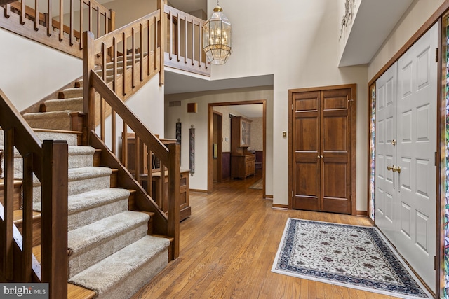 entrance foyer with a towering ceiling, wood finished floors, baseboards, a notable chandelier, and stairs