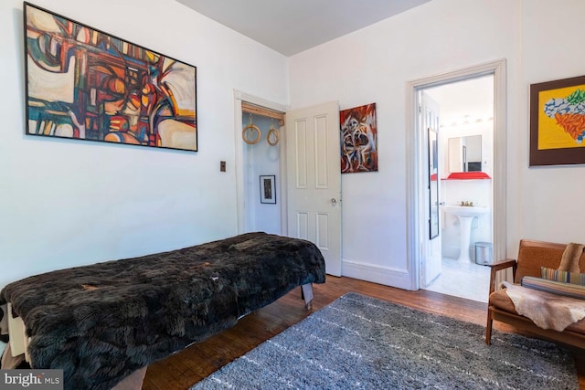 bedroom with connected bathroom, baseboards, a sink, and wood finished floors