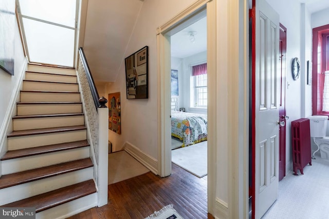 staircase featuring baseboards, wood finished floors, and lofted ceiling