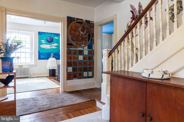foyer entrance with stairway, radiator, baseboards, and wood finished floors
