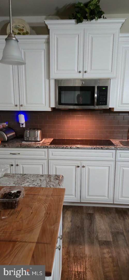 24840 Mistletoe Dr, Georgetown, DE 19947 - kitchen featuring black electric stovetop, stainless steel microwave, white cabinets, tasteful backsplash, and dark stone countertops