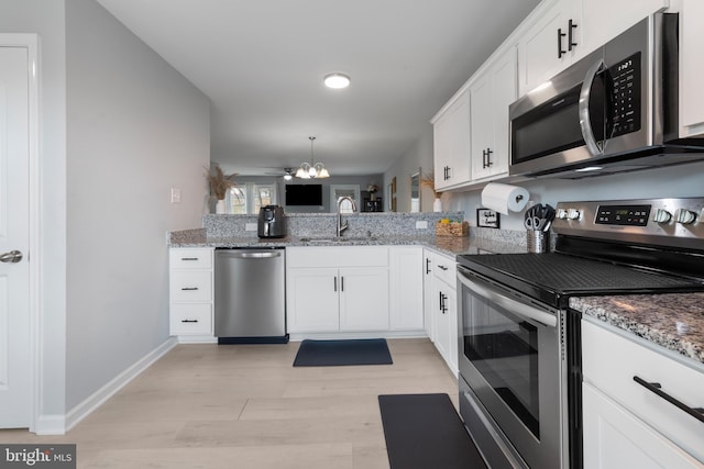 kitchen featuring an inviting chandelier, light stone countertops, light wood-style floors, a sink, and stainless steel appliances