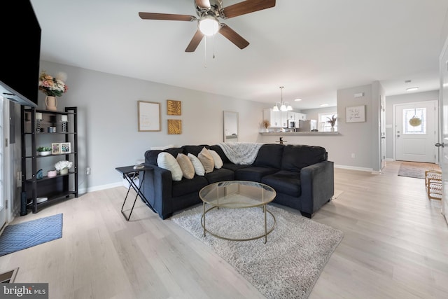 living area featuring baseboards, light wood finished floors, and ceiling fan with notable chandelier
