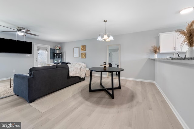 living room with baseboards, ceiling fan with notable chandelier, and light wood-type flooring