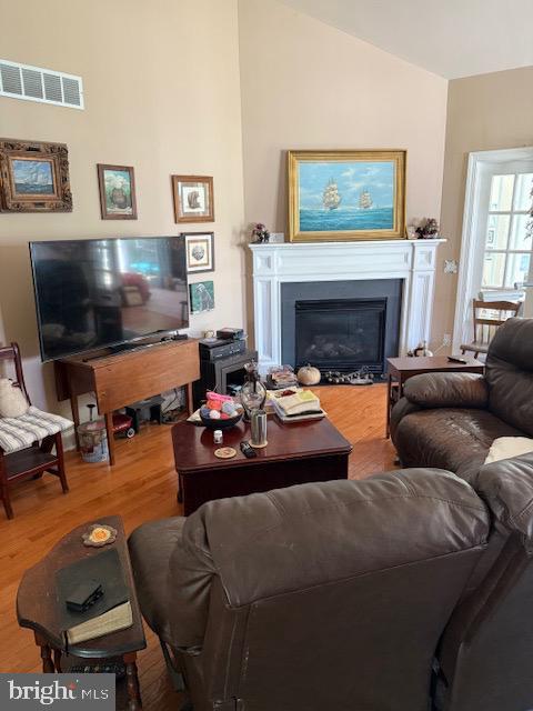 living area featuring visible vents, a glass covered fireplace, wood finished floors, and lofted ceiling