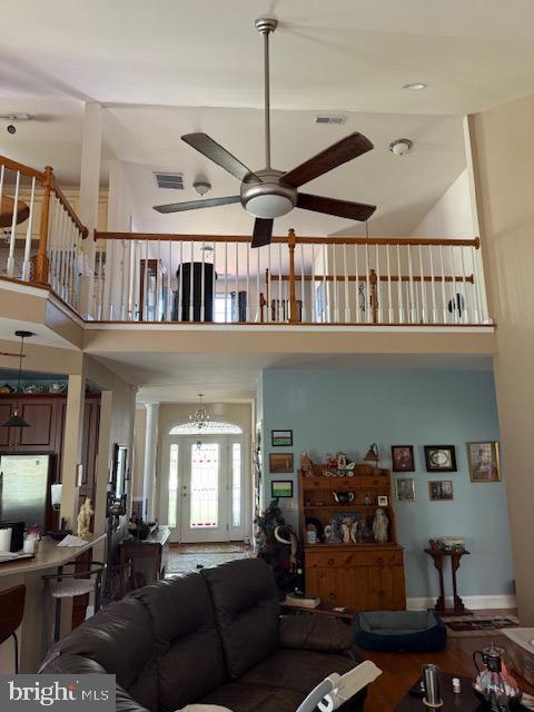living area with ceiling fan, visible vents, and a towering ceiling