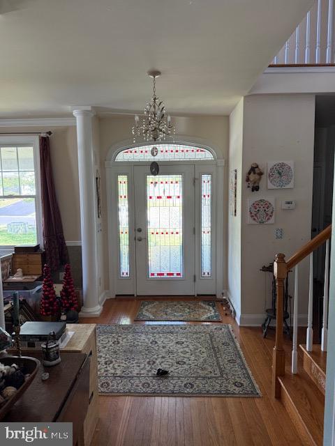 entryway featuring an inviting chandelier, wood finished floors, baseboards, stairway, and ornate columns