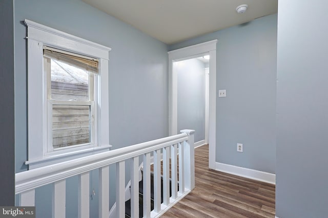 corridor with baseboards, wood finished floors, and an upstairs landing