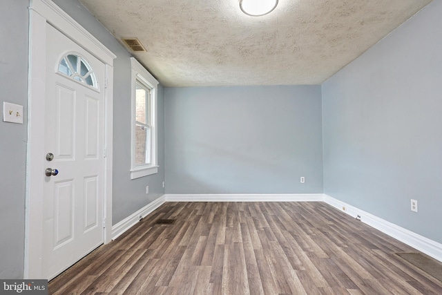 foyer with baseboards, a textured ceiling, wood finished floors, and visible vents