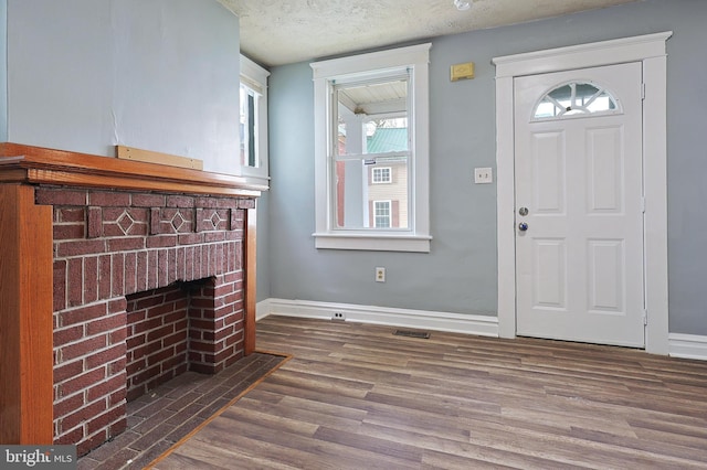 foyer entrance with baseboards, a textured ceiling, wood finished floors, and a fireplace