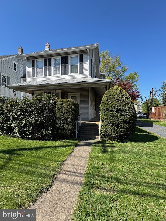 view of front of house with covered porch, a chimney, and a front yard