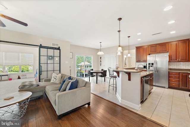 living area featuring ceiling fan, a barn door, recessed lighting, light wood-type flooring, and visible vents
