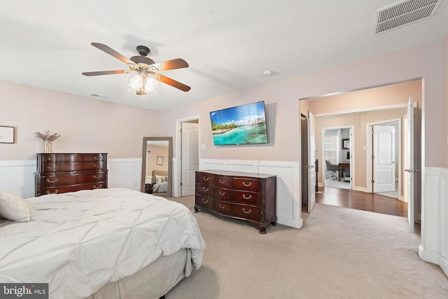 bedroom with visible vents, ceiling fan, a wainscoted wall, and light carpet