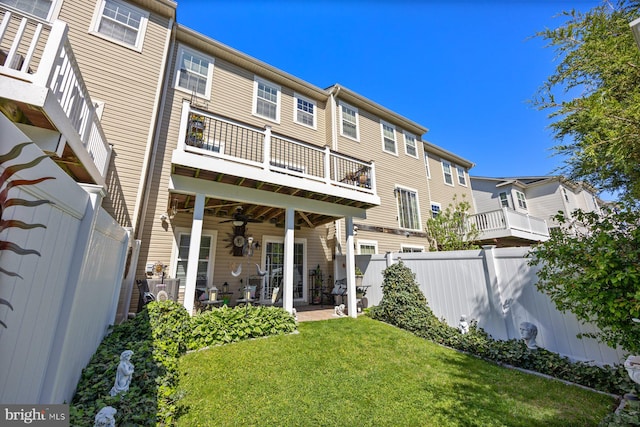 rear view of property with ceiling fan, a balcony, a patio, a fenced backyard, and a yard