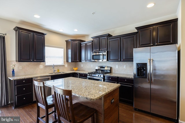 kitchen with light stone countertops, dark wood-type flooring, a center island, a sink, and stainless steel appliances