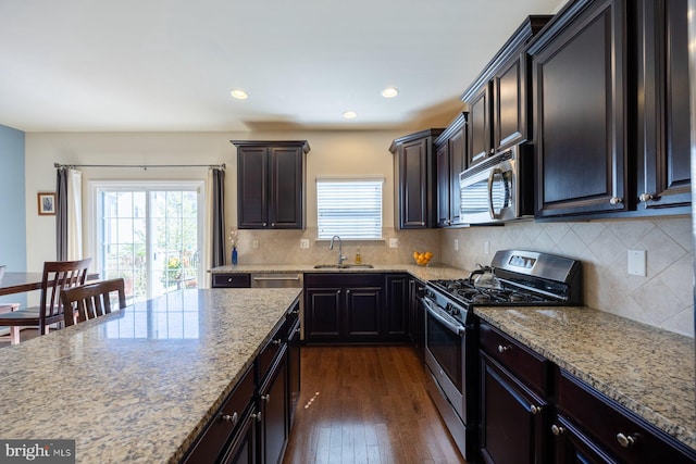 kitchen featuring backsplash, stainless steel appliances, light stone countertops, and a sink