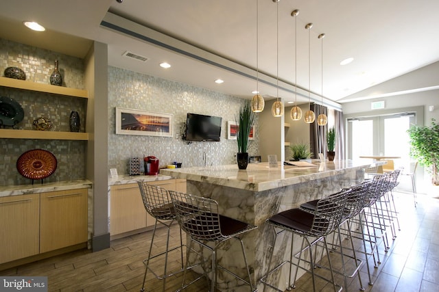 kitchen featuring visible vents, decorative backsplash, lofted ceiling, a kitchen bar, and light wood-style flooring