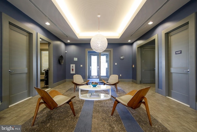 living area with baseboards, a tray ceiling, french doors, and light wood-style floors