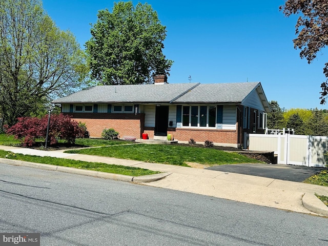 single story home with a front lawn, aphalt driveway, fence, a chimney, and brick siding